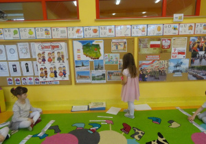 Dziewczynka stoi pod tablicą i przygląda się odkrytym ilustracją.